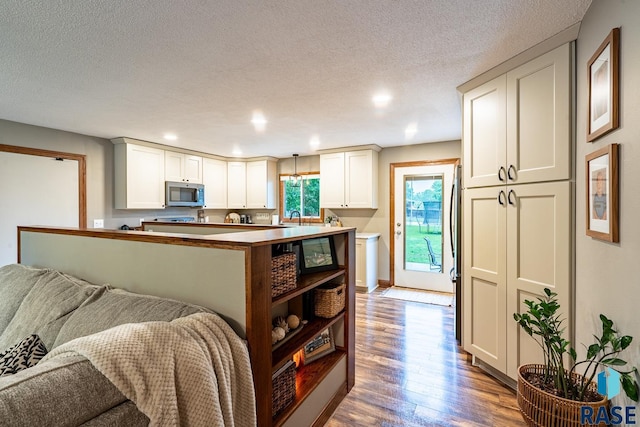 kitchen featuring stainless steel microwave, open floor plan, wood finished floors, a sink, and a textured ceiling