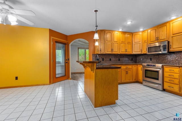 6700 W Snowberry Cir, Sioux Falls, SD 57106 - kitchen featuring stainless steel appliances, arched walkways, a breakfast bar area, decorative backsplash, and dark countertops
