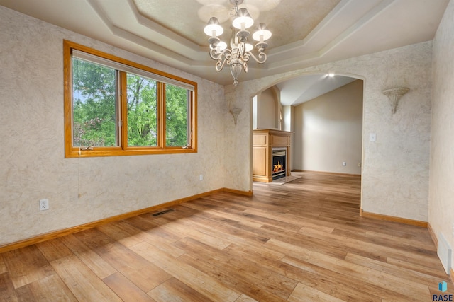 6700 W Snowberry Cir, Sioux Falls, SD 57106 - unfurnished living room with arched walkways, light wood finished floors, a raised ceiling, a warm lit fireplace, and a chandelier