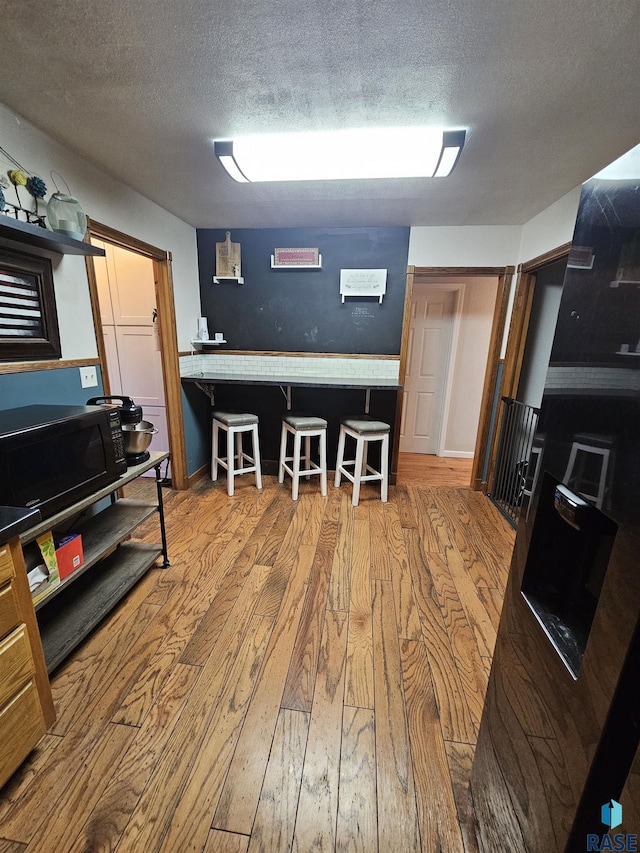 511 N 3rd St, Emery, SD 57332 - kitchen with hardwood / wood-style floors, black microwave, a textured ceiling, a breakfast bar, and baseboards