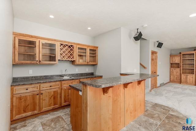 1817 W Ashton Trl, Brandon, SD 57005 - kitchen featuring a breakfast bar area, glass insert cabinets, a sink, recessed lighting, and light stone finish floors