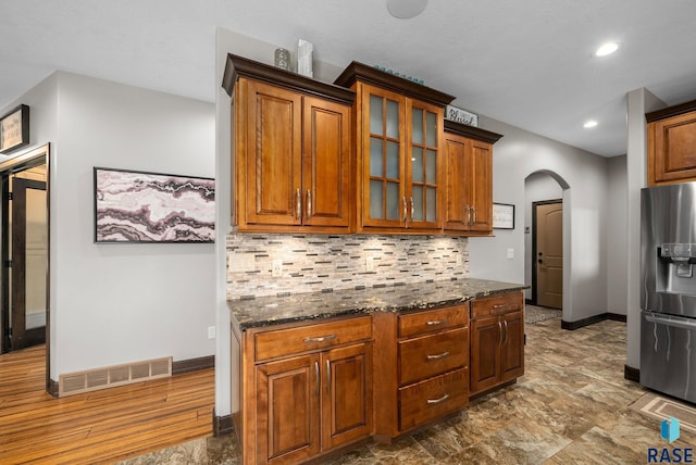 1301 S Hyannis Port Ln, Sioux Falls, SD 57106 - kitchen featuring stainless steel refrigerator with ice dispenser, arched walkways, baseboards, backsplash, and dark stone counters