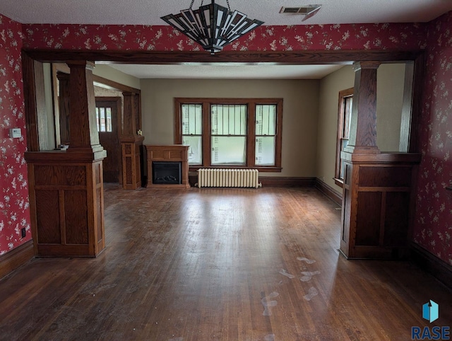 302 E 19th St, Sioux Falls, SD 57105 - unfurnished living room featuring radiator heating unit, decorative columns, wood finished floors, wallpapered walls, and baseboards