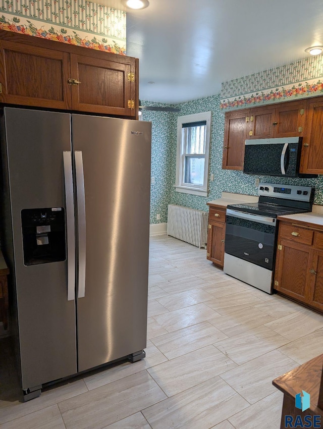 302 E 19th St, Sioux Falls, SD 57105 - kitchen featuring stainless steel appliances, wallpapered walls, radiator, brown cabinetry, and light countertops