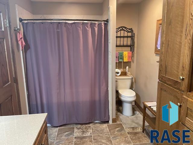 218 S Douglas St, Inwood, IA 51240 - full bath with toilet, vanity, stone finish floors, and a shower with shower curtain