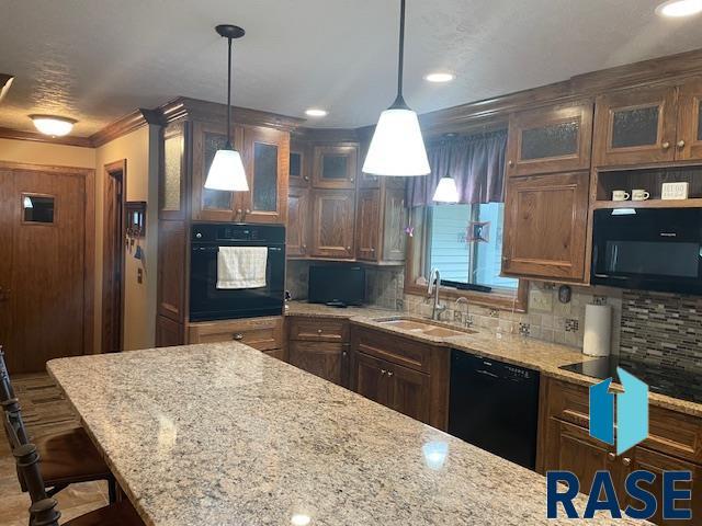 218 S Douglas St, Inwood, IA 51240 - kitchen with black appliances, a sink, backsplash, a breakfast bar area, and light stone countertops