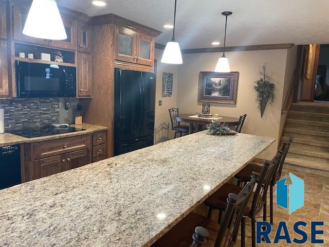218 S Douglas St, Inwood, IA 51240 - kitchen with black appliances, a breakfast bar, glass insert cabinets, decorative backsplash, and light stone counters