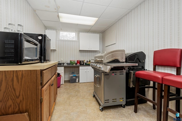 7005 W Strabane Trl, Sioux Falls, SD 57106 - kitchen featuring black microwave, wallpapered walls, light floors, white cabinets, and a drop ceiling