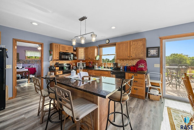 48484 262nd St, Valley Springs, SD 57068 - kitchen with black appliances, light wood-type flooring, backsplash, brown cabinetry, and a breakfast bar