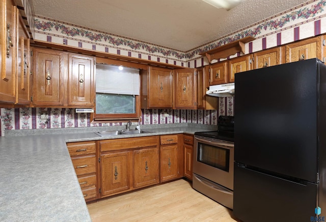 6905 W 6th St, Sioux Falls, SD 57107 - kitchen with freestanding refrigerator, stainless steel electric range, under cabinet range hood, wallpapered walls, and brown cabinetry