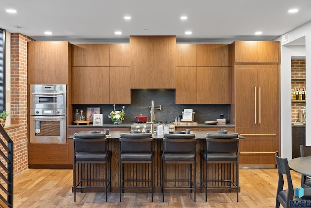 151 E 4th Pl Unit 102, Sioux Falls, SD 57104 - kitchen with stainless steel double oven, light wood-type flooring, a kitchen island with sink, decorative backsplash, and recessed lighting