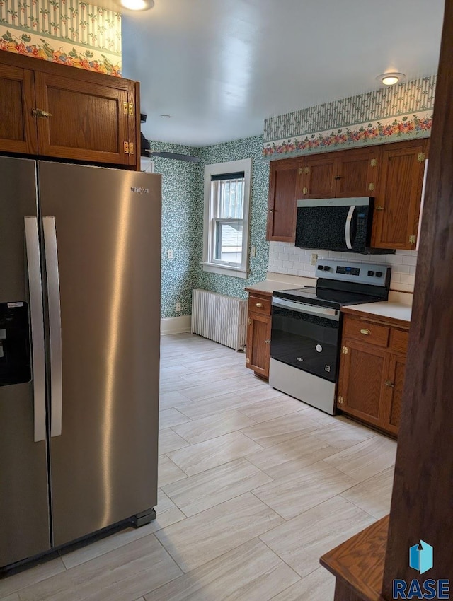 302 E 19th St, Sioux Falls, SD 57105 - kitchen featuring appliances with stainless steel finishes, radiator heating unit, wallpapered walls, light countertops, and brown cabinets