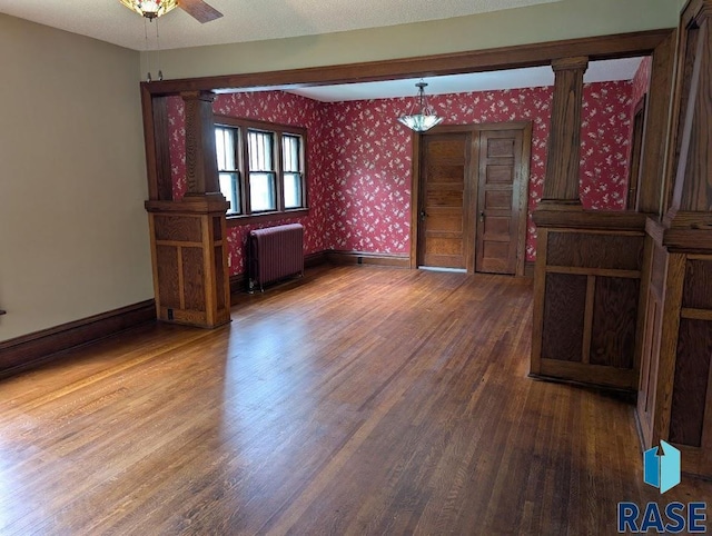 302 E 19th St, Sioux Falls, SD 57105 - empty room featuring radiator heating unit, wood finished floors, wallpapered walls, baseboards, and decorative columns