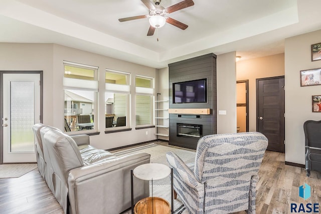 2604 S Ronell Cir, Sioux Falls, SD 57106 - living room featuring light wood-type flooring, a ceiling fan, a tray ceiling, a large fireplace, and baseboards