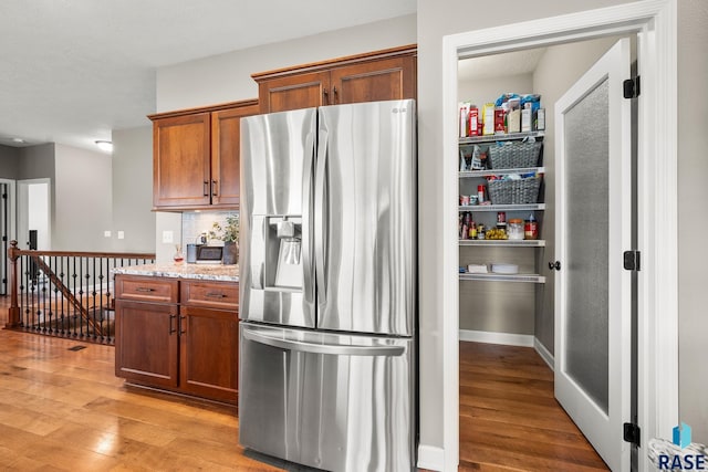 8216 W 51st St, Sioux Falls, SD 57106 - kitchen with stainless steel fridge, light wood-style flooring, brown cabinetry, and light stone counters