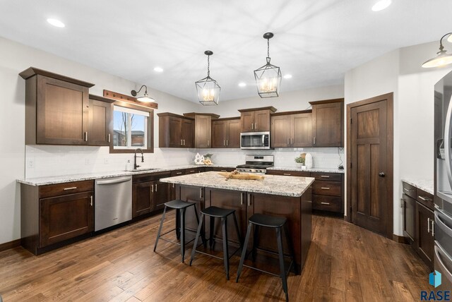 2101 S Meadowview Ave, Sioux Falls, SD 57110 - kitchen with appliances with stainless steel finishes, dark brown cabinetry, decorative backsplash, a sink, and a center island