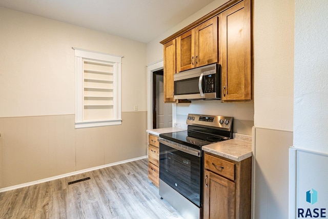 108 S Sycamore Ave, Sioux Falls, SD 57110 - kitchen with appliances with stainless steel finishes, brown cabinets, light wood-type flooring, wainscoting, and light countertops
