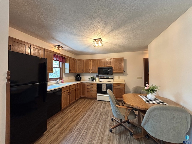 421 E 2nd St, Miller, SD 57362 - kitchen with black appliances, wood finished floors, light countertops, brown cabinetry, and a textured ceiling