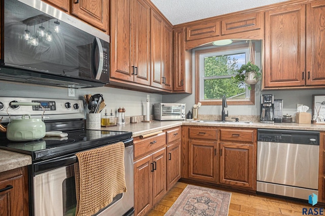 300 W 3rd St, Tea, SD 57064 - kitchen with appliances with stainless steel finishes, brown cabinets, light countertops, light wood finished floors, and a textured ceiling