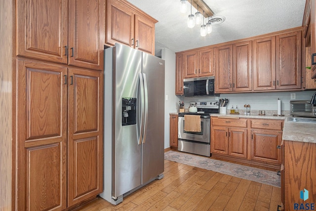 300 W 3rd St, Tea, SD 57064 - kitchen featuring appliances with stainless steel finishes, light wood-style flooring, brown cabinets, and a textured ceiling