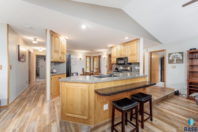 4808 S Shields Ave, Sioux Falls, SD 57103 - kitchen with black microwave, light brown cabinets, range, light wood-style flooring, and a breakfast bar area