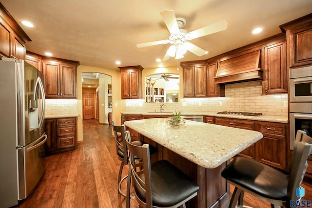 6811 E Split Rock Cir, Sioux Falls, SD 57110 - kitchen with appliances with stainless steel finishes, premium range hood, a ceiling fan, arched walkways, and backsplash