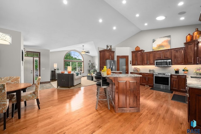 4400 E Aster Cir, Sioux Falls, SD 57103 - kitchen with stainless steel appliances, light wood-style floors, vaulted ceiling, a ceiling fan, and a kitchen breakfast bar