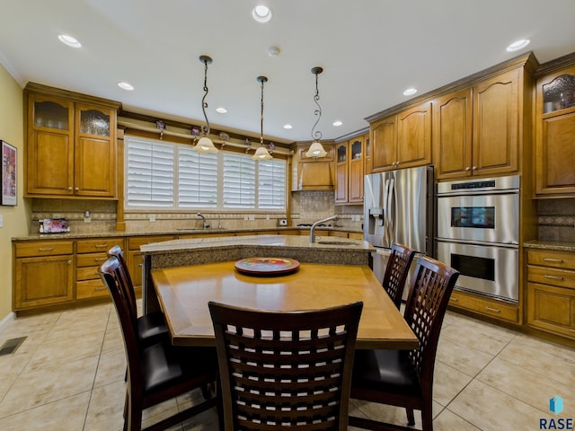 18 S Elkjer Cir, Sioux Falls, SD 57103 - kitchen featuring stainless steel appliances, light tile patterned floors, brown cabinetry, decorative backsplash, and glass insert cabinets