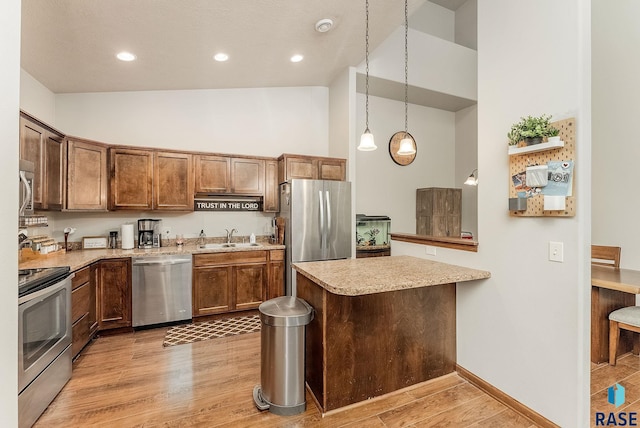4005 S Grand Slam Ave, Sioux Falls, SD 57110 - kitchen with appliances with stainless steel finishes, a towering ceiling, light wood-type flooring, a peninsula, and decorative light fixtures