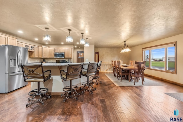 705 Railway St, Canistota, SD 57012 - kitchen with stainless steel appliances, a kitchen bar, light brown cabinetry, dark wood-type flooring, and a textured ceiling