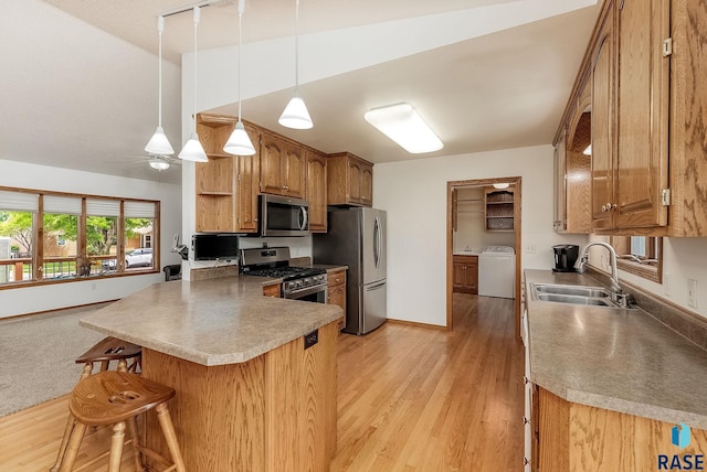 303 E 11th St, Dell Rapids, SD 57022 - kitchen featuring appliances with stainless steel finishes, washer / clothes dryer, a peninsula, brown cabinetry, and a breakfast bar area