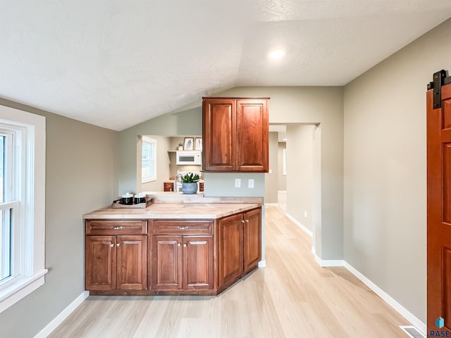 340 N Juniper Ave, Parker, SD 57053 - kitchen with light wood finished floors, light countertops, brown cabinetry, vaulted ceiling, and a barn door