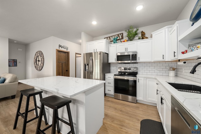 5402 S Bahnson Ave, Sioux Falls, SD 57108 - kitchen with appliances with stainless steel finishes, a kitchen bar, backsplash, light wood-type flooring, and white cabinets
