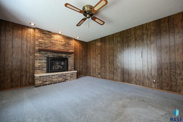 2312 E 19th St, Sioux Falls, SD 57103 - unfurnished living room featuring a ceiling fan, wood walls, carpet flooring, a fireplace, and a textured ceiling
