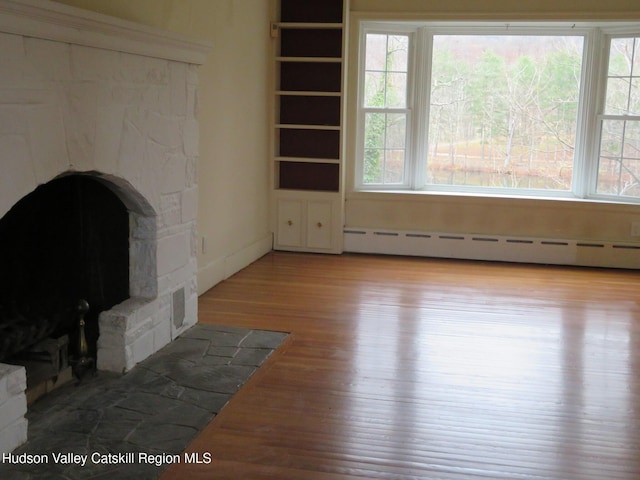 unfurnished living room with a baseboard radiator, a stone fireplace, and light hardwood / wood-style floors