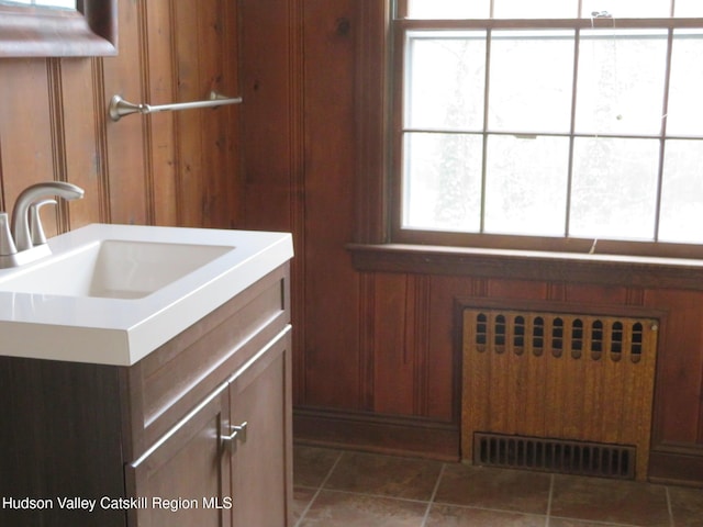 bathroom featuring wooden walls, radiator heating unit, plenty of natural light, and sink