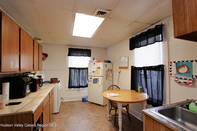 kitchen with a drop ceiling, white appliances, and sink