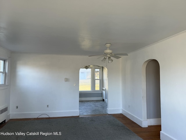 empty room with dark hardwood / wood-style floors, ceiling fan, crown molding, and radiator