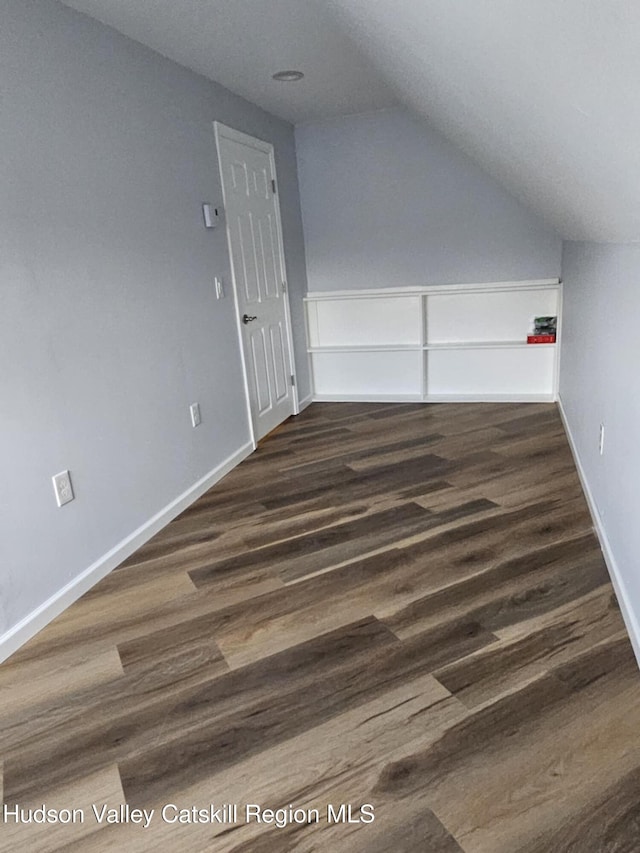 additional living space with baseboards, vaulted ceiling, and dark wood-type flooring