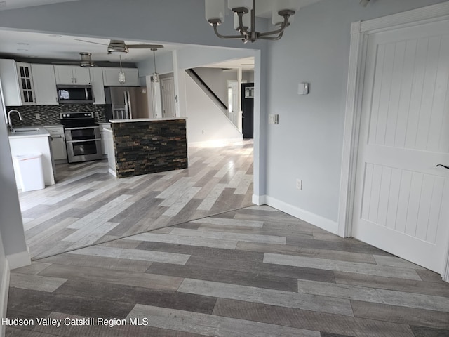 kitchen featuring tasteful backsplash, white cabinets, light wood-style floors, stainless steel appliances, and a notable chandelier