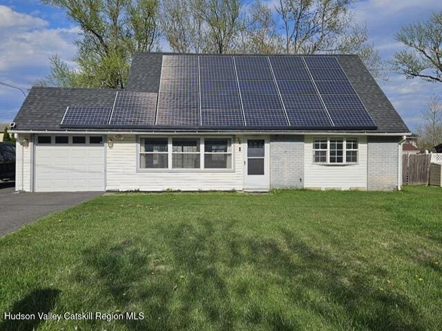 exterior space featuring a front lawn, a garage, driveway, solar panels, and fence