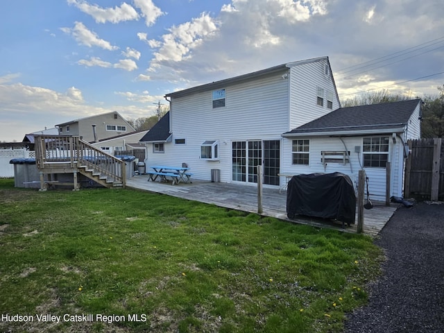 rear view of house with a lawn, a wooden deck, stairs, and fence