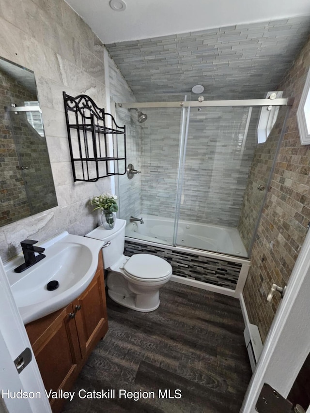 bathroom with tile walls, vanity, tiled shower / bath, toilet, and wood finished floors