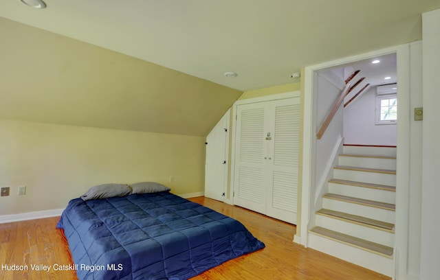 bedroom with baseboards, wood finished floors, vaulted ceiling, and a closet