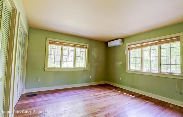 spare room with baseboards, a wall unit AC, a wealth of natural light, and hardwood / wood-style flooring
