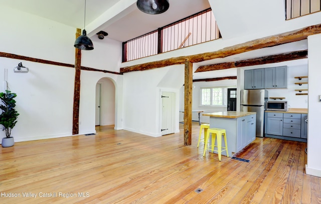 kitchen featuring a towering ceiling, a breakfast bar area, arched walkways, stainless steel appliances, and light wood-type flooring