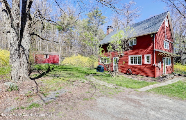 exterior space with an outdoor structure, a shingled roof, and a chimney