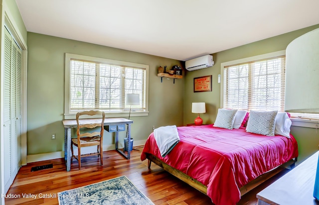 bedroom with multiple windows, a closet, a wall mounted air conditioner, and wood finished floors