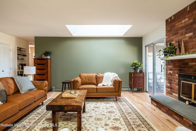 living area with a baseboard heating unit, baseboards, light wood-style flooring, a fireplace, and a skylight