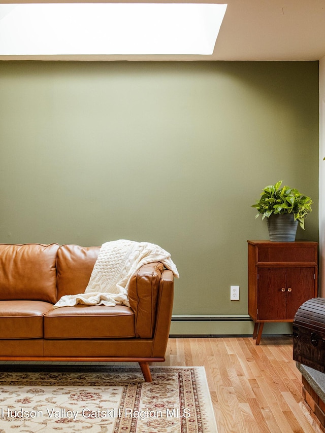 living area featuring light wood-style flooring, a skylight, a baseboard heating unit, and baseboards